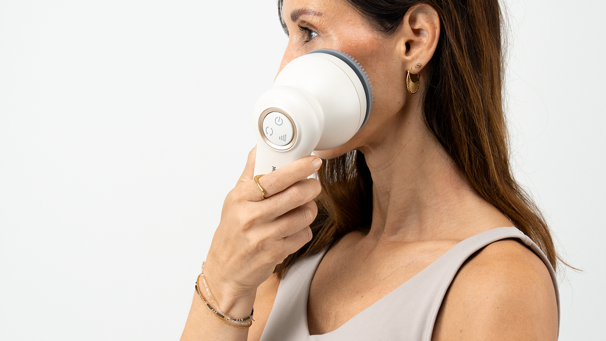 Vrouw houdt de Venen Engel Glow Brush met grijs opzetstuk tegen haar wang